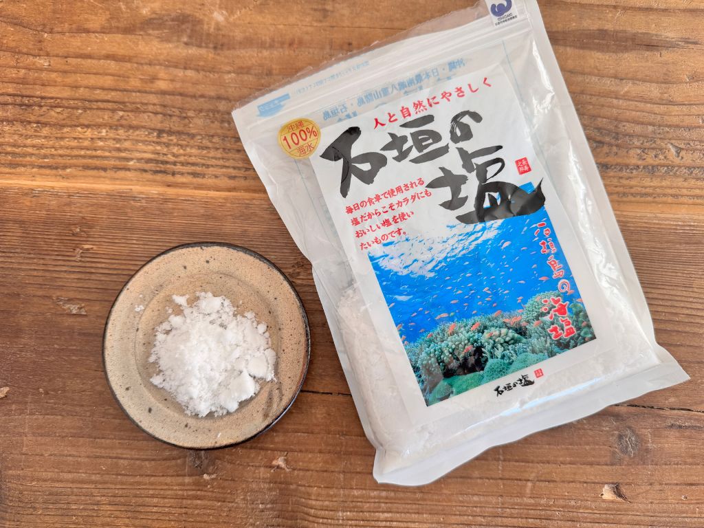 沖縄県石垣島の「石垣の塩」のパッケージと、小皿に盛られたしっとりとした粒状の塩の写真。