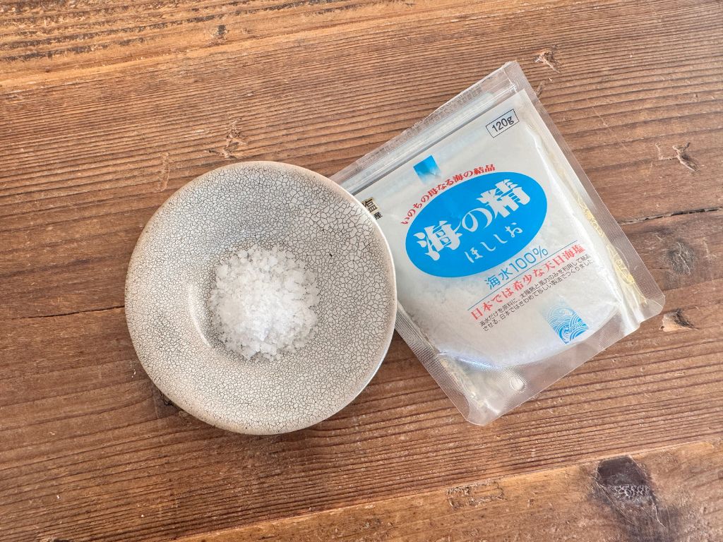 伊豆大島の完全天日塩「海の精 ほししお(青)」のパッケージと、小皿に盛られたザクザクとした結晶状の塩の写真。