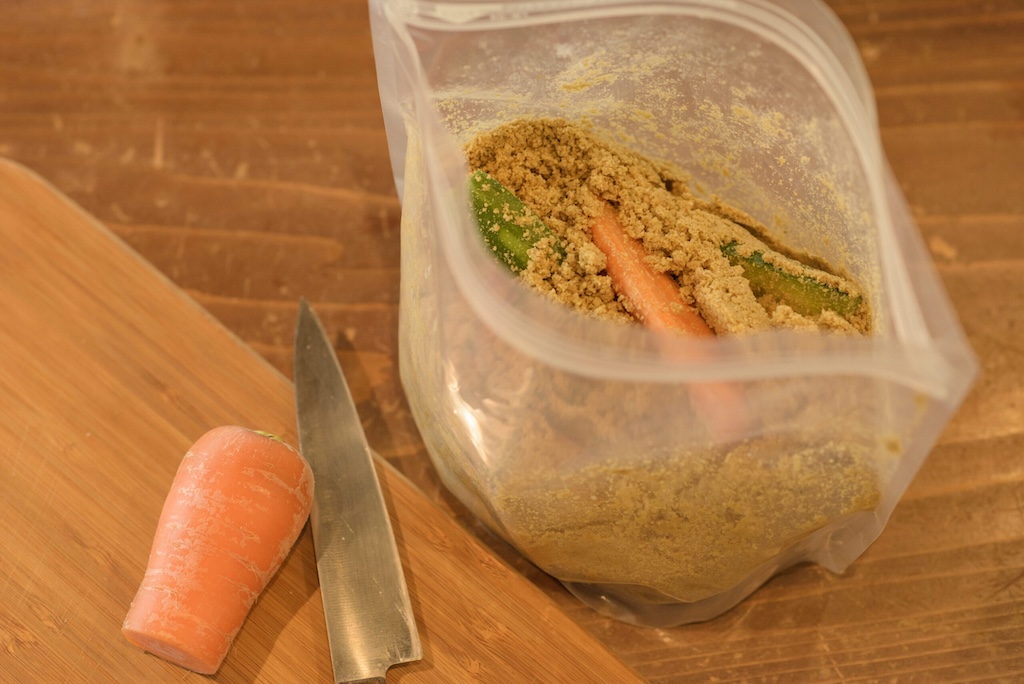 竹ぬか床の専用ジップ袋に、切ったきゅうりとにんじんを差し込んでいる様子。