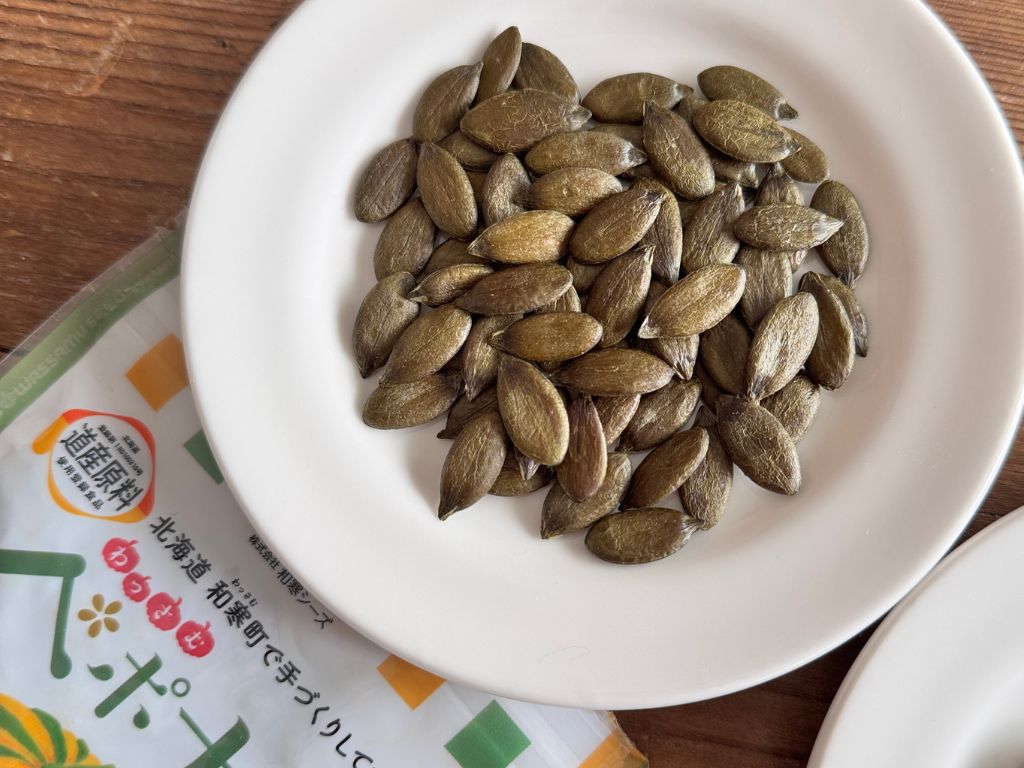 北海道和寒町産の希少な国産カボチャの種「ペポナッツ」。砂糖断ち中の甘いもの欲求を抑えるミネラル補給おやつとして、白い皿に盛られた様子とパッケージ。