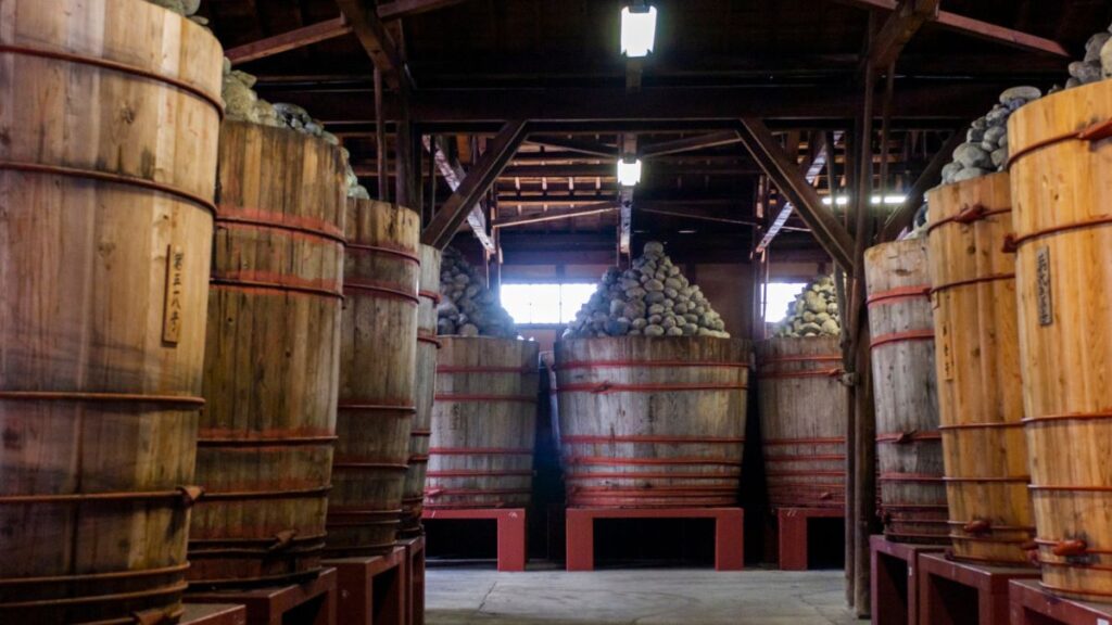 伝統的な味噌蔵の内部。大きな木桶が並び、上には重石が山のように積まれている