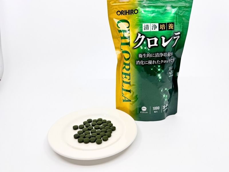 オリヒロ清浄培養クロレラのパッケージと粒。緑のジッパー付きパウチに1000粒入り。白い皿に並べた深緑色の丸い粒。
