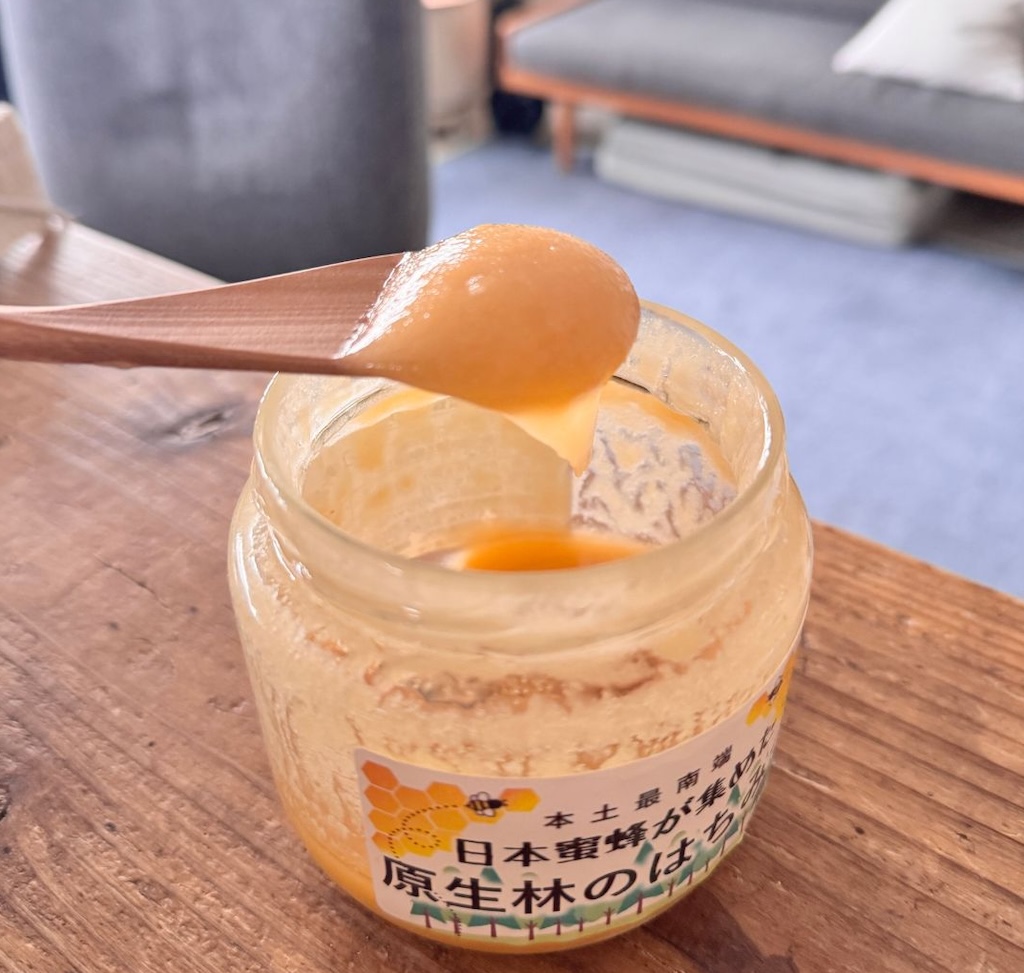 原生林のはちみつ瓶から木のスプーンで結晶化したクリーム状の蜂蜜をすくい上げている様子